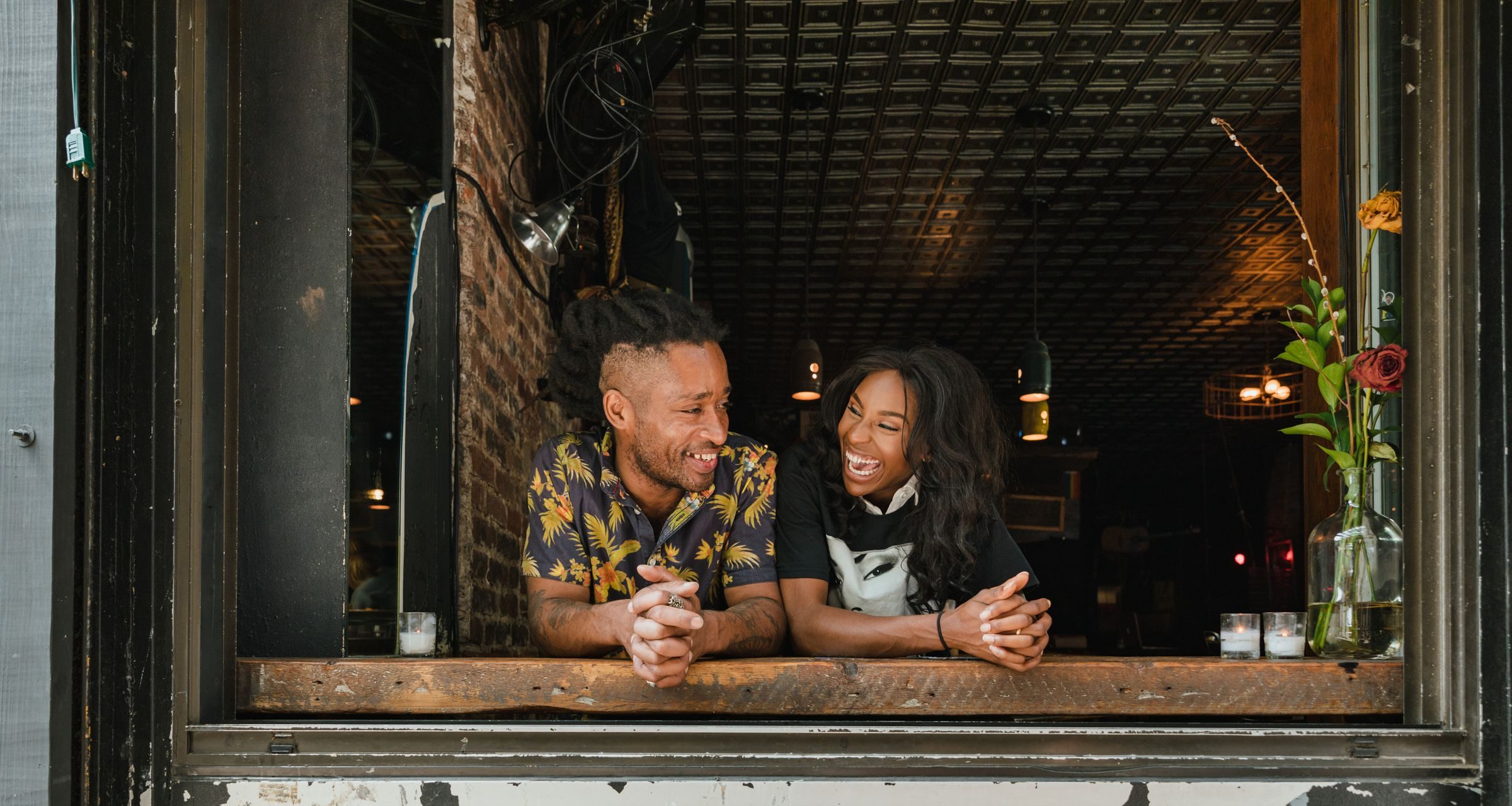 Two business owners smiling from the window of their shop